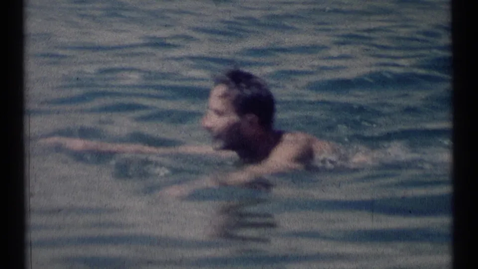 Closer 1973 8mm view of a dark-haired adult man swimming breaststroke in a Montana lake.