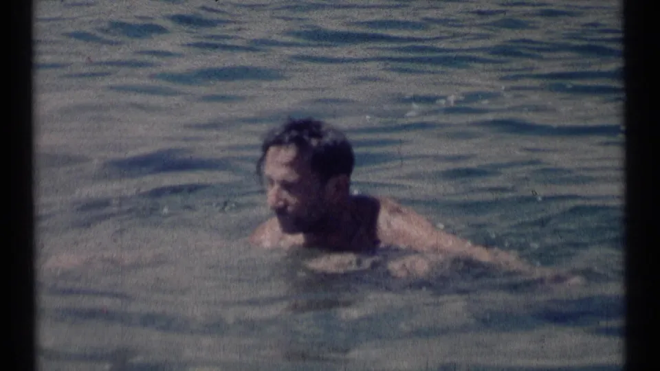 A close home-movie frame shows the adult swimmer's head and shoulders above the Montana lake water.