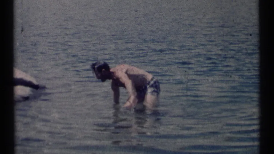 A man bends and wades in shallow lake water in the Montana wilderness clip, with soft exposure and visible 8mm grain.