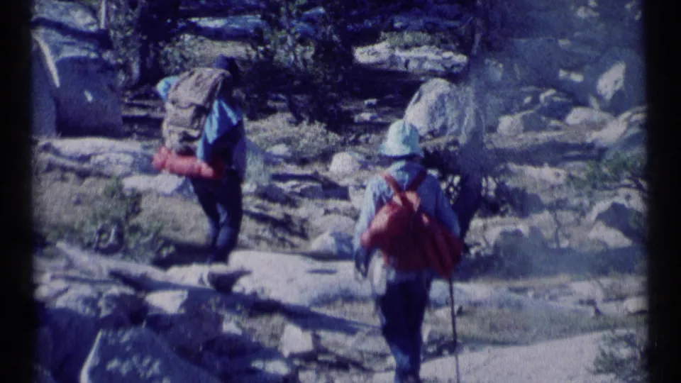 Two hikers with backpacks move through rocky Scapegoat Wilderness terrain in the 1973 8mm home movie.