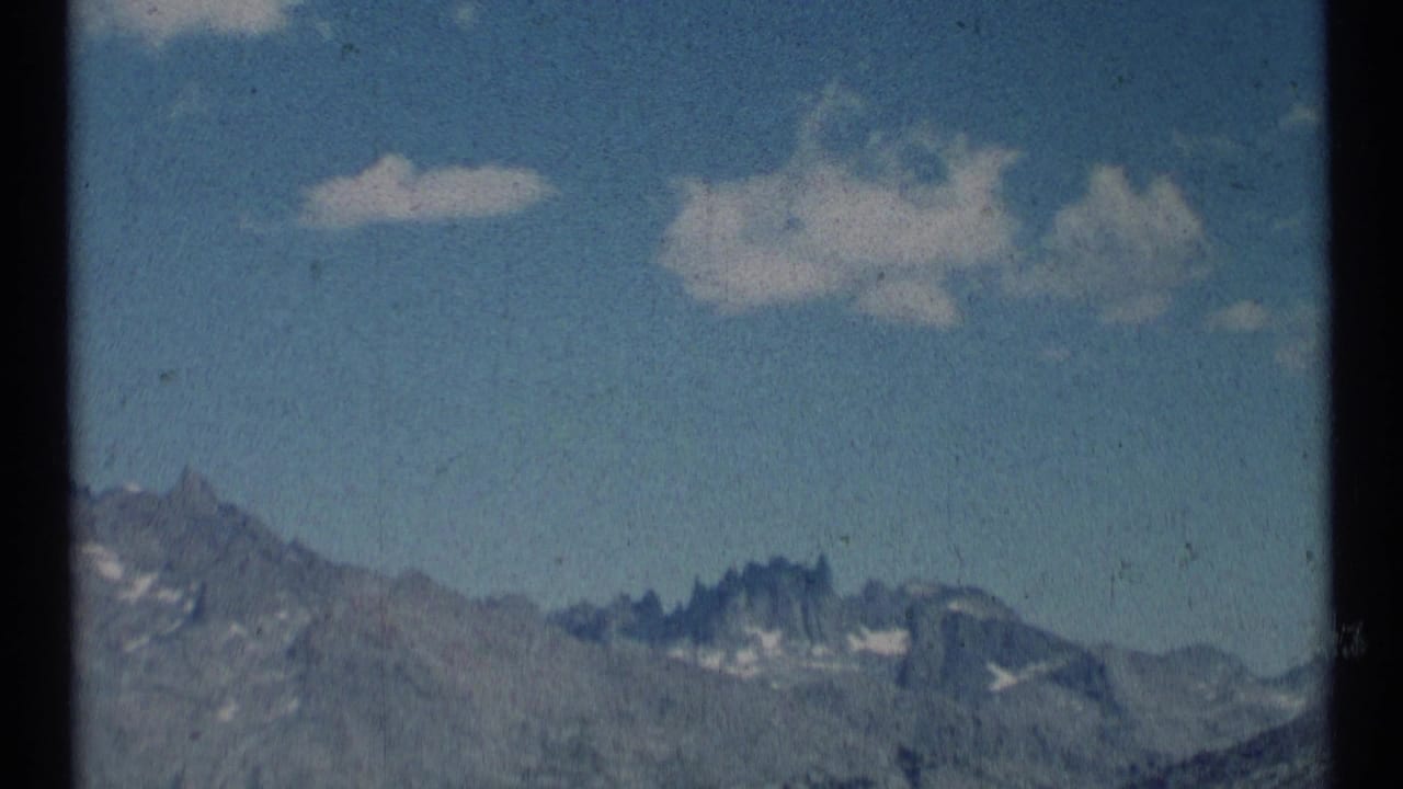 Distant rocky mountain peaks with snow patches beneath a blue sky and small clouds.