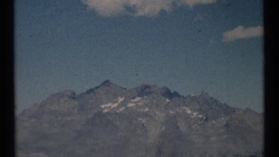 Scapegoat Wilderness 1973 8mm frame with a rocky summit, snow-marked ridge, and open blue sky.