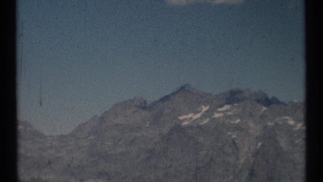 Distant rocky mountain ridge beneath a pale blue sky with small snow patches.