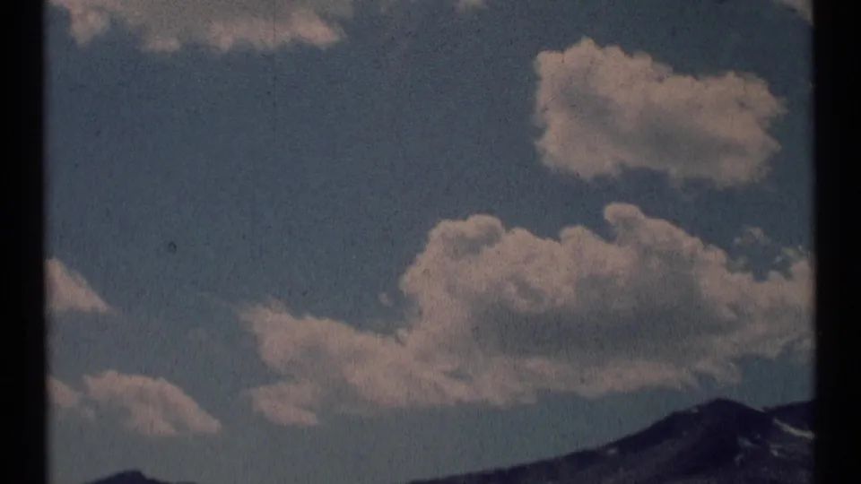 1973 8mm Montana wilderness view with broad clouds drifting above a mountain peak near the right edge of the frame.