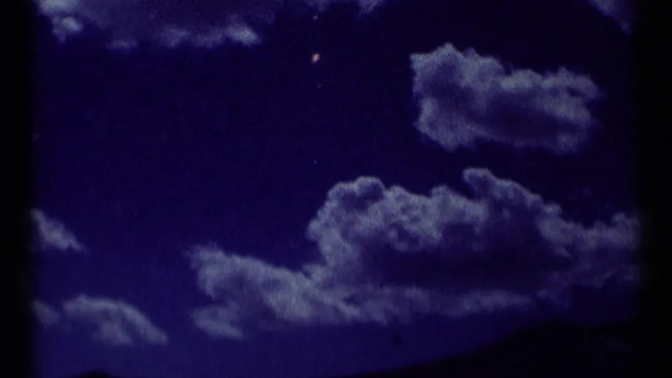 1973 Montana wilderness frame with a purple exposure shift, scattered clouds, and a low dark mountain silhouette.