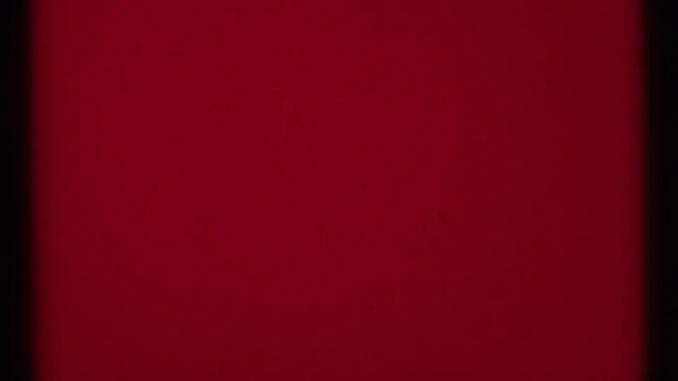 Red-tinted 8mm frame area with gate edges, grain, and faint surface marks, likely part of the clip ending.