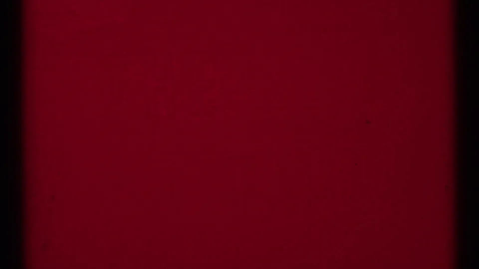 Closing red-tinted 8mm frame from the 1973 clip, showing dark borders, grain, and faint scratches without visible subjects.