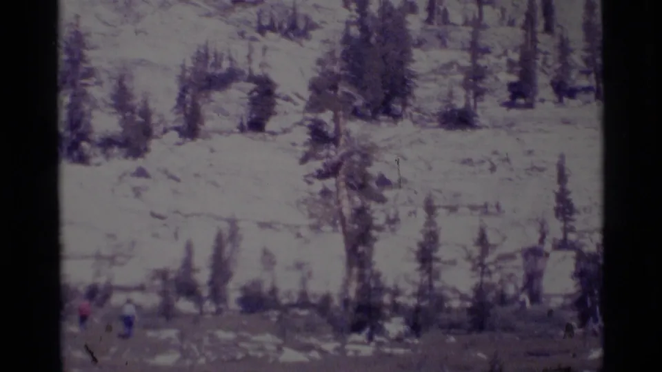 Wide 1975 8mm view of hikers on rocky ground in the Minaret Wilderness, with sparse pines and hazy light.