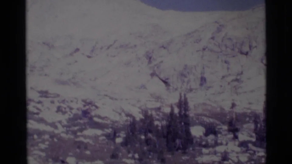 Wide 8mm home-movie view of a snowy mountain landscape with evergreen trees, supported by the supplied 1975 Minaret Wilderness metadata.