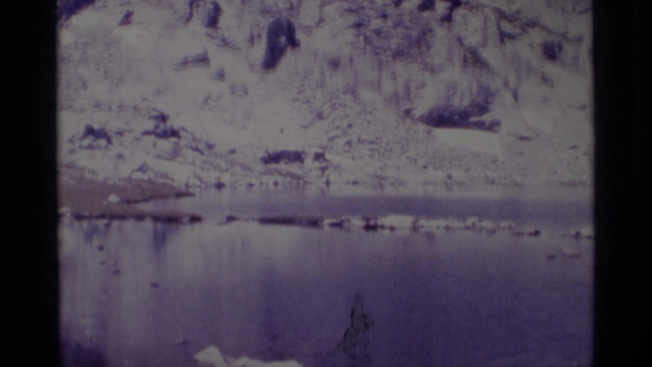 Reservoir water below pale rocky slopes with snow patches.