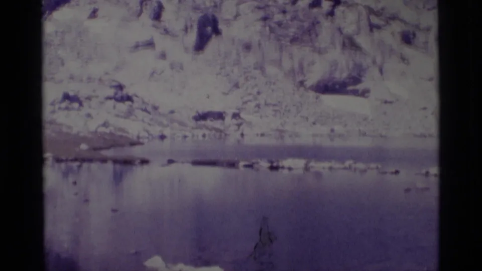 Faded 8mm view of a calm reservoir beneath rugged, snow-dusted slopes in Minaret Wilderness, California.