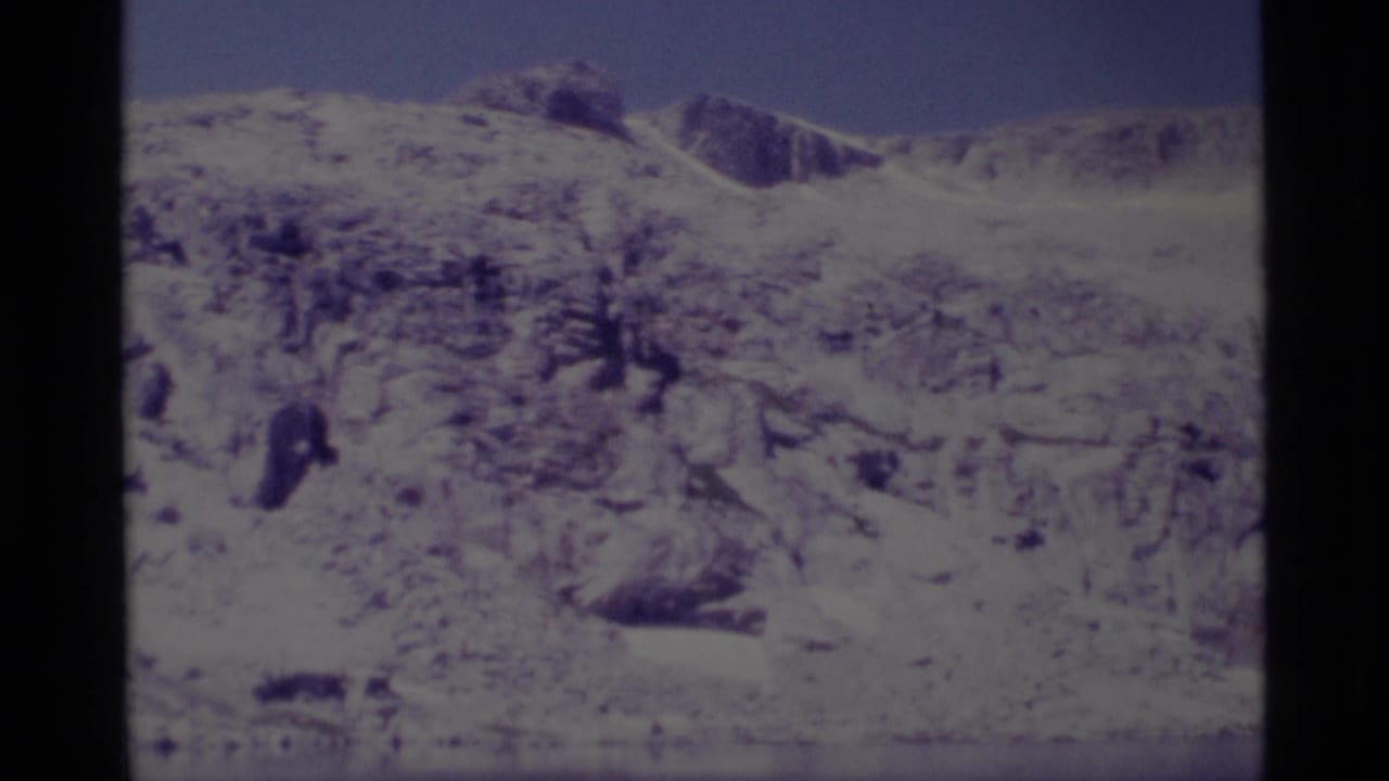 1975 8mm Minaret Wilderness view of a snow-dusted rocky slope under blue sky, with sparse dark trees in the foreground.