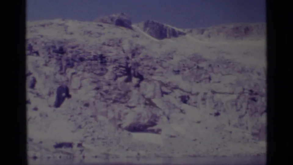 1975 8mm Minaret Wilderness view of a snow-dusted rocky slope under blue sky, with sparse dark trees in the foreground.