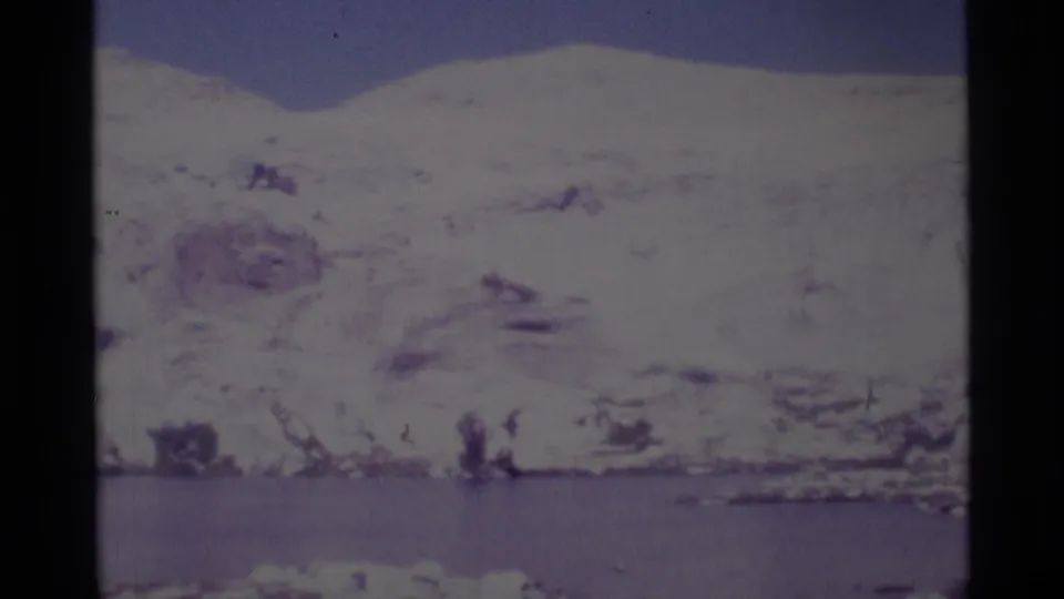 A faded 8mm frame shows a snow-bright mountain slope over lake water in Minaret Wilderness, California.