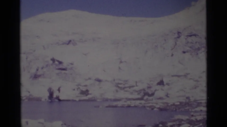 The final frame holds on the snow-covered mountain and calm lake, with soft focus and faded 8mm color.