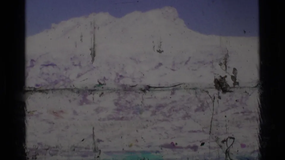 Final 1975 8mm view of snow-covered Minaret Wilderness mountains over a lake, with prominent film scratches and worn frame edges.