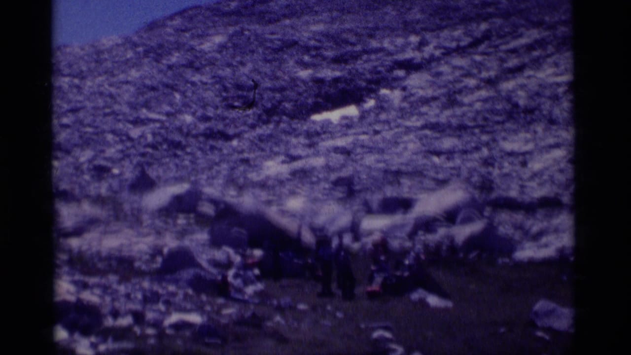 Small group of hikers gathered near boulders on a rocky mountain slope.