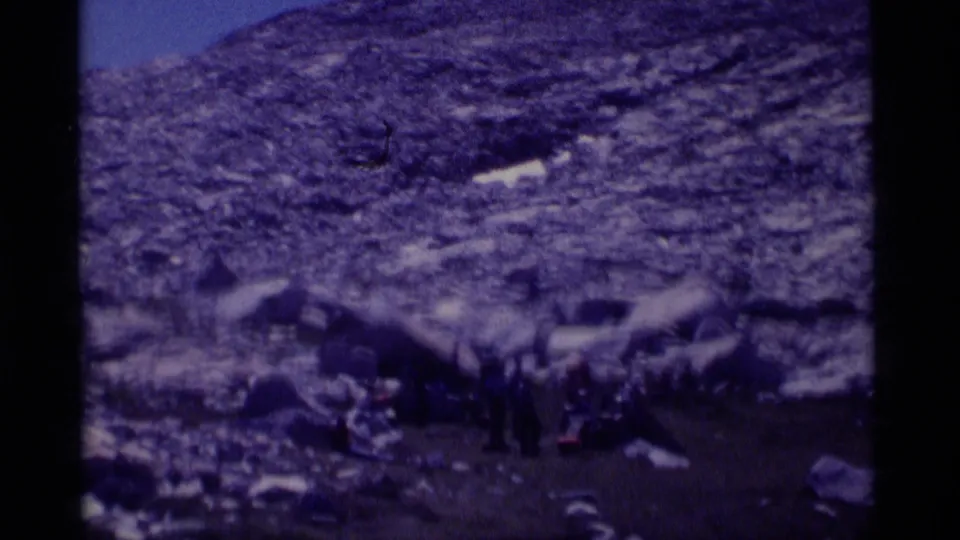 In the Minaret Wilderness, a distant group of hikers appears gathered with gear among large boulders on a rocky slope.