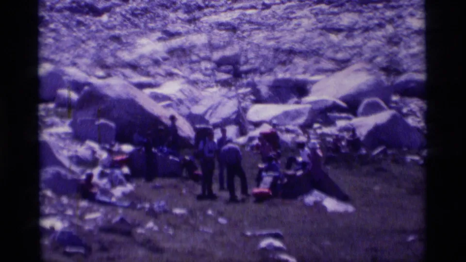 A 1975 8mm view shows hikers standing and sitting with backpacks and loose gear among boulders in the Minaret Wilderness.