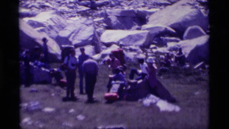 Closer 8mm frame of the Minaret Wilderness group resting, with several hikers, backpacks, and gear arranged beside large boulders.