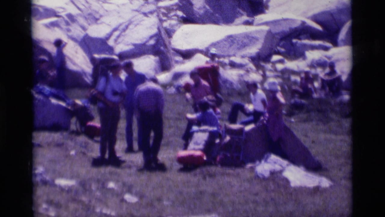 1975 8mm frame of hikers resting on a grassy patch among large boulders in the Minaret Wilderness area of California.