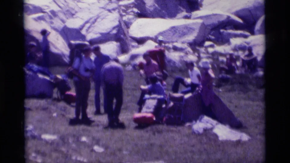 1975 8mm frame of hikers resting on a grassy patch among large boulders in the Minaret Wilderness area of California.