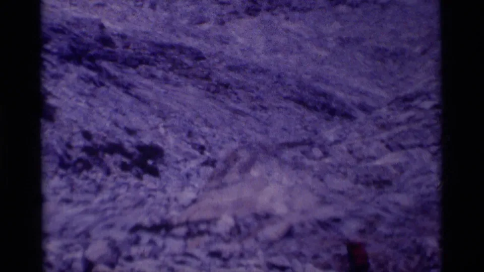 Soft, grainy 8mm frame of steep rocky alpine ground with scattered snow patches in the California wilderness setting.