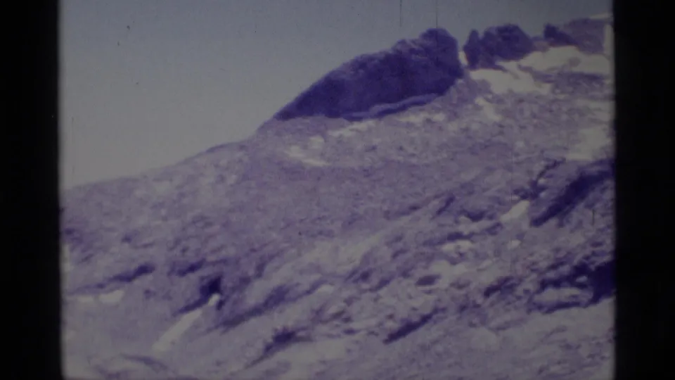 Wide 1975 8mm view of Minaret Wilderness slopes with rocky terrain, pale sky, and snow patches in the distance.