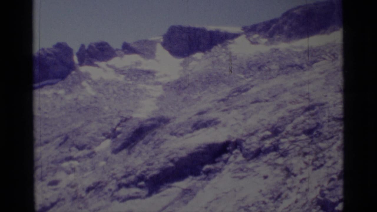 1975 8mm view in Minaret Wilderness showing rough alpine rock, scattered snow, and dark ridgeline outcrops.