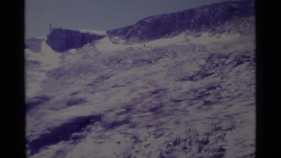 1975 8mm Minaret Wilderness frame with a dark rock outcrop, snow band, and loose rocky ground on a mountain slope.
