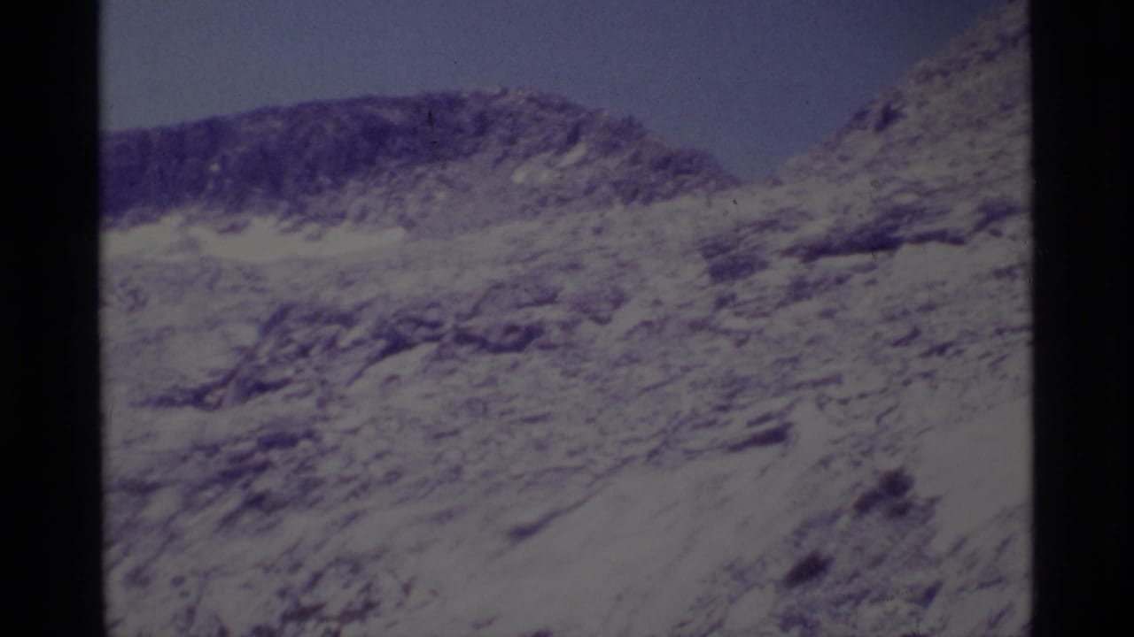 1975 8mm frame of a rugged Minaret Wilderness rocky ridge with sparse vegetation and a blue sky.