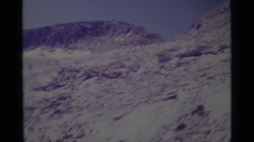 1975 8mm frame of a rugged Minaret Wilderness rocky ridge with sparse vegetation and a blue sky.