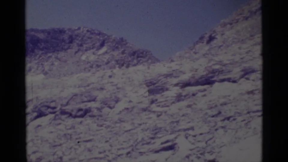 1975 home-movie frame showing a rocky California wilderness slope with sparse scrub and clear sky.