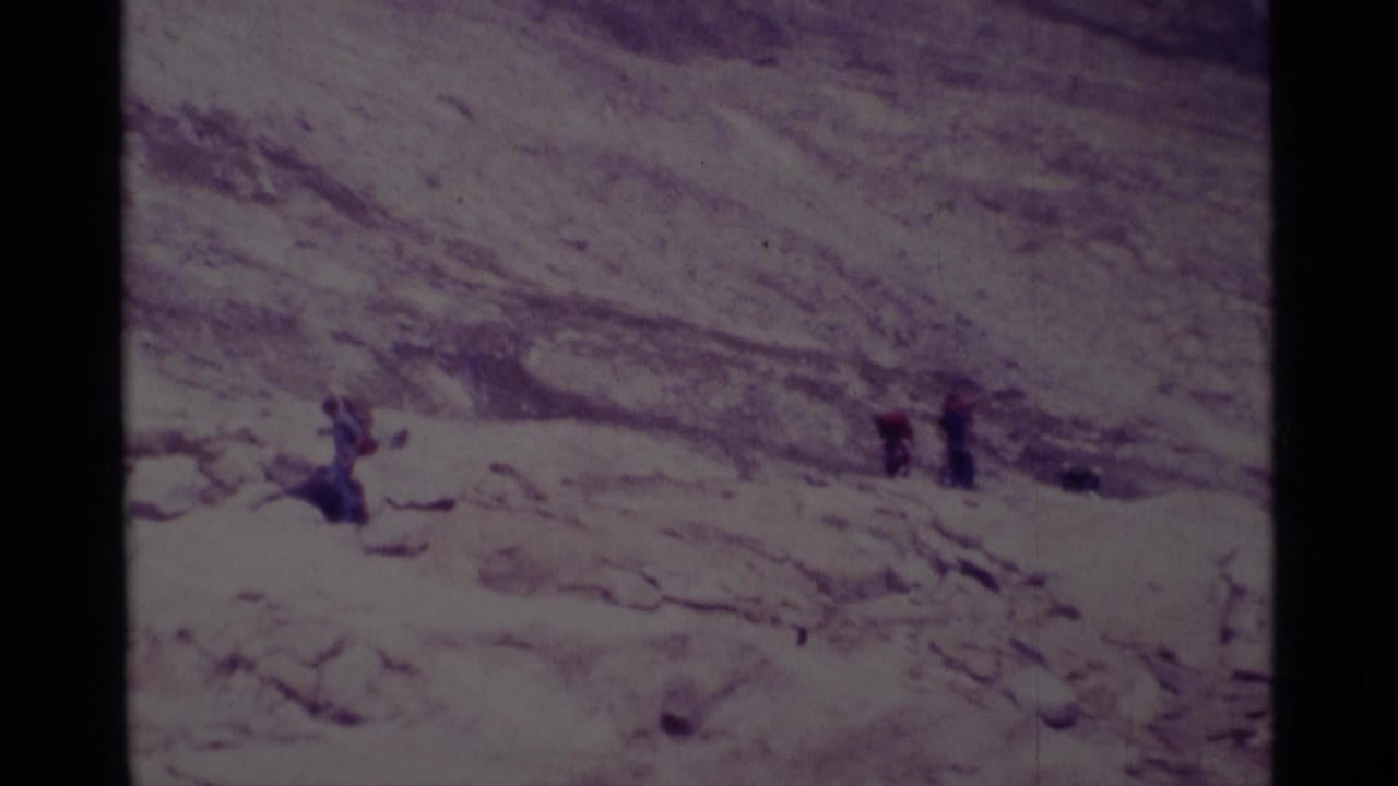1975 8mm frame from Minaret Wilderness showing small hikers moving across a sunlit rocky slope in a dry mountain landscape.