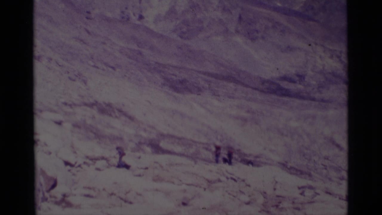 Small hikers on a rocky slope with broad mountain terrain behind them.