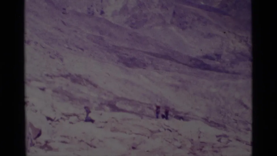 1975 8mm frame from Minaret Wilderness with distant hikers set against pale rock, dry slopes, and a hazy mountain backdrop.