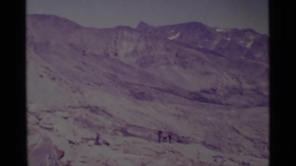Wide 1975 8mm view of Minaret Wilderness terrain, with distant hikers near the bottom of the frame below ridged mountains.