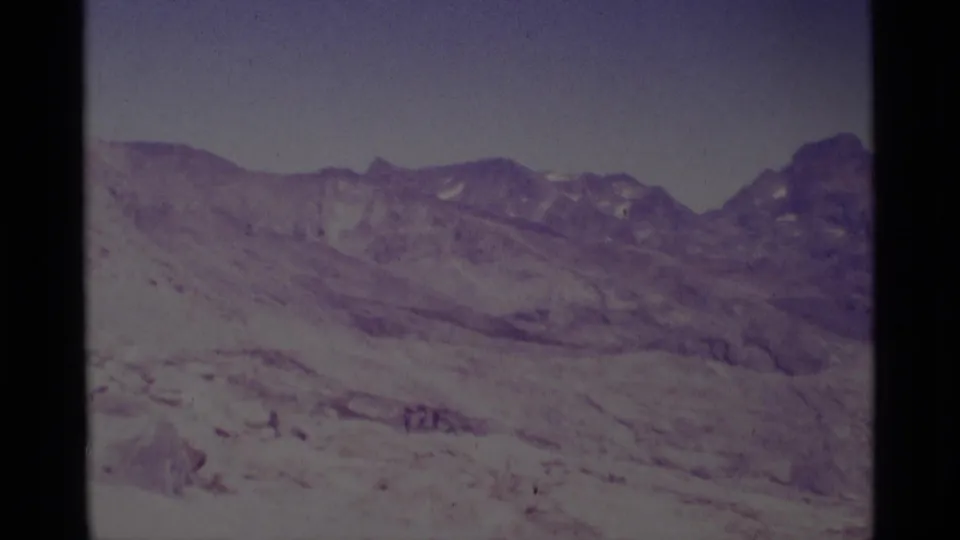 Minaret Wilderness landscape on 8mm film, showing a broad snow-covered basin, rocky ridge, and faint distant figures.