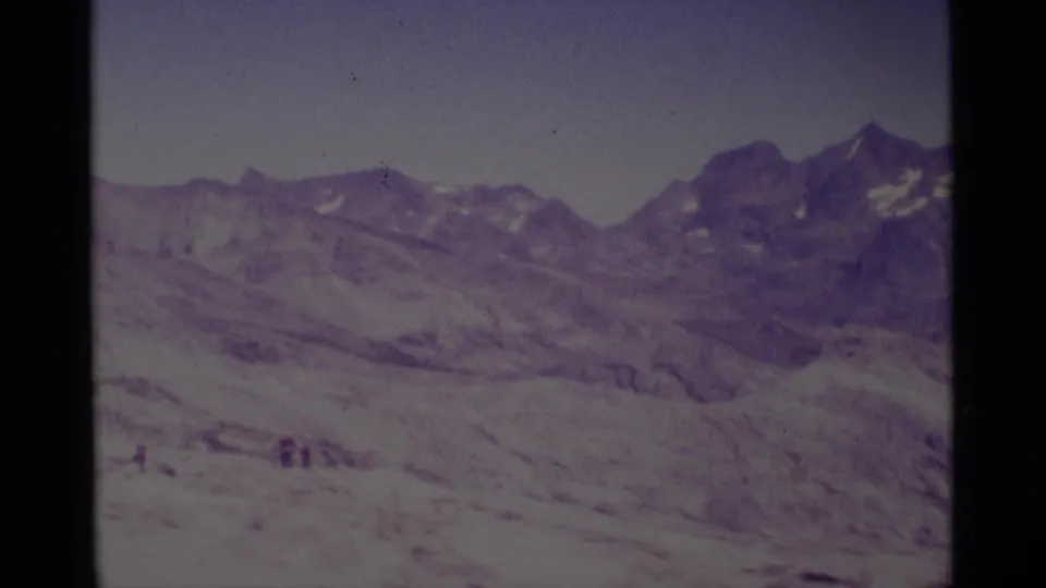 1975 California wilderness frame with jagged snow-dusted peaks, a wide snowfield, and small distant people near the foreground.