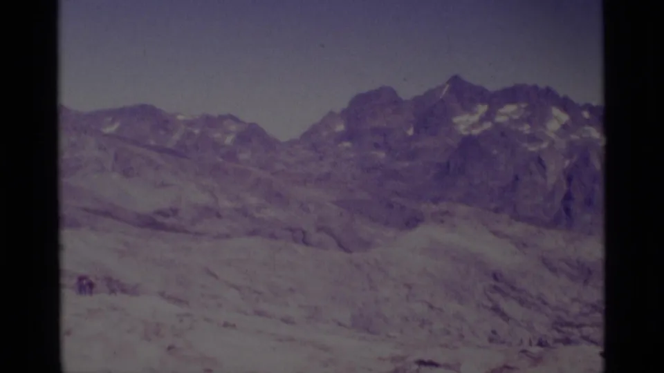 Minaret Wilderness 8mm frame showing snow-covered ridges, darker rocky peaks, and small distant people on the lower slope.