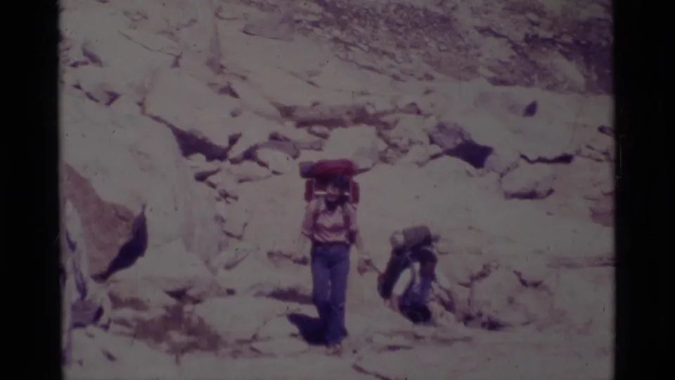 Two backpackers, one carrying a red pack, move through rocky Minaret Wilderness terrain in 1975 8mm footage.