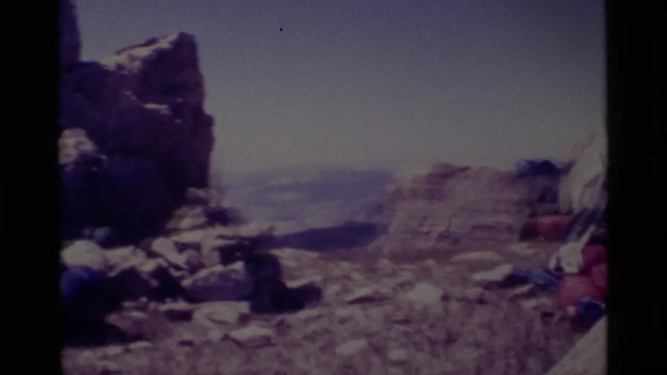 Minaret Wilderness rest spot with backpacks or gear near a rocky outcrop and a hazy mountain vista in faded 8mm color.