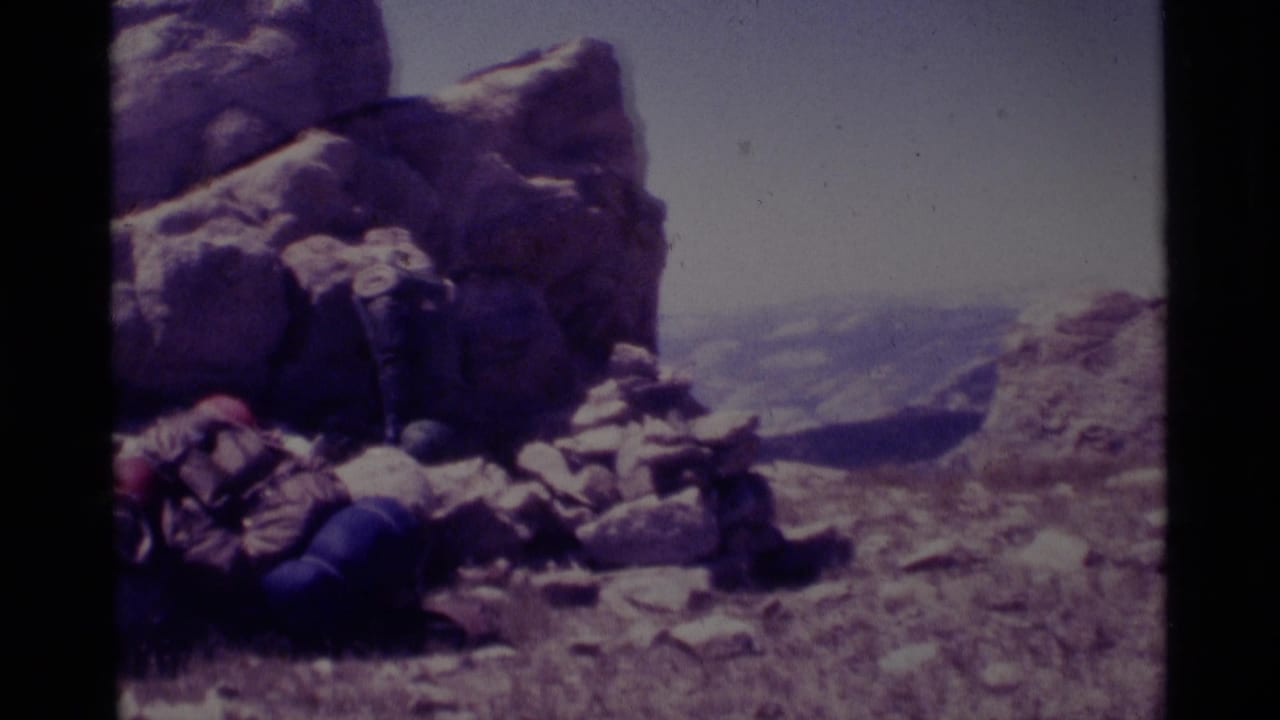 1975 8mm frame of hikers resting near a stone cairn and large summit rocks in Minaret Wilderness, California.