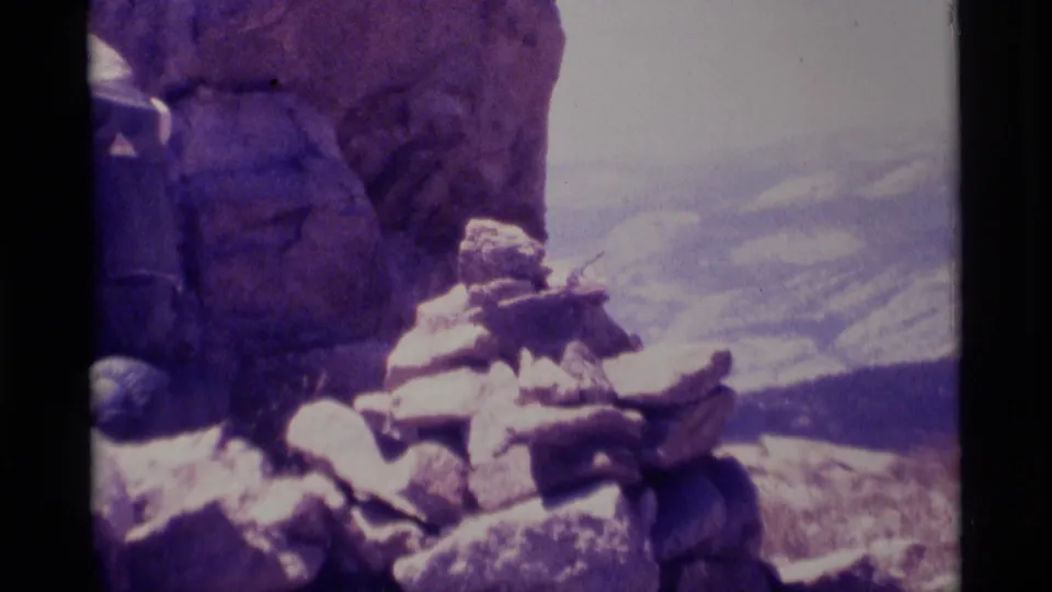 A soft 8mm frame shows hikers seated among summit rocks in Minaret Wilderness with distant mountain haze behind them.