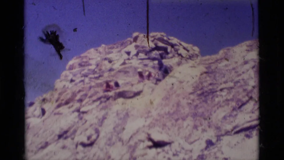 A rocky Sierra Nevada ridge fills the frame under blue sky, with visible dust and scratches from the 8mm film scan.