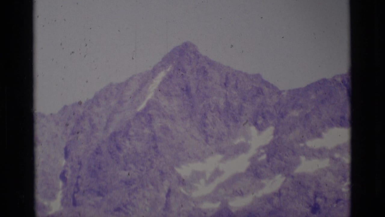 Jagged mountain peak with pale snow patches and dark film borders.