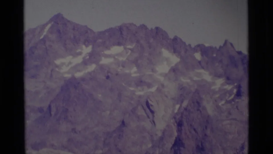 1975 8mm view of rugged Minaret Wilderness peaks with snow patches and faded purple film color.