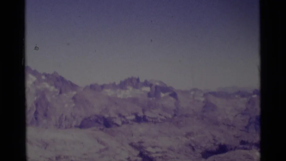 Wide 1975 home-movie panorama of California alpine ridges and distant mountain forms beneath open sky.