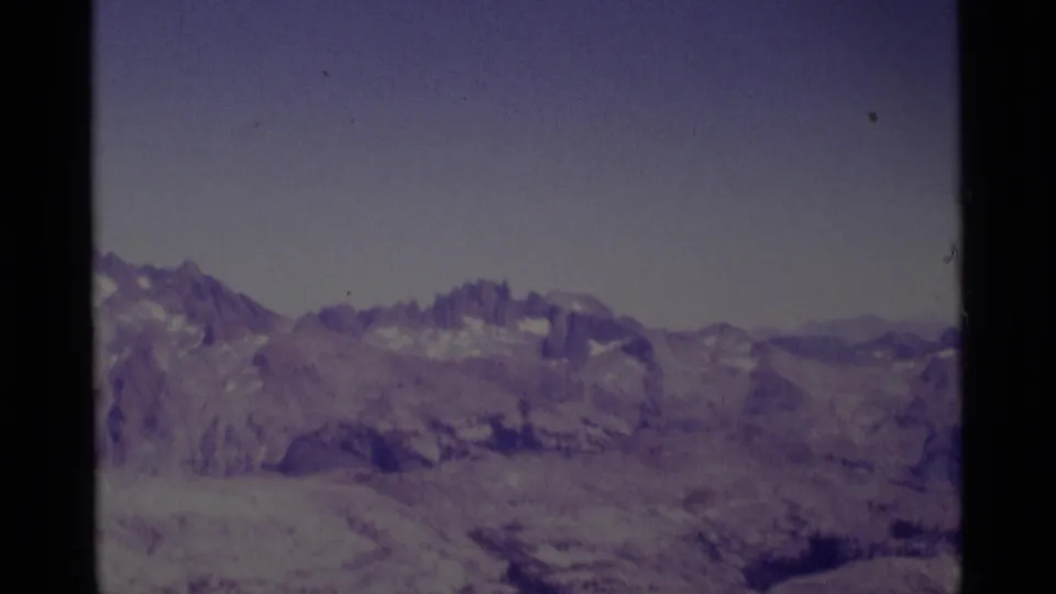 Faded 8mm frame of Minaret Wilderness terrain with distant ridges, rocky slopes, and pale sky.