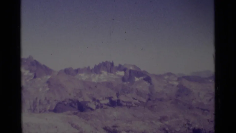 1975 8mm view of the Minaret Wilderness area, showing distant jagged Sierra Nevada peaks and muted snow patches under a pale sky.